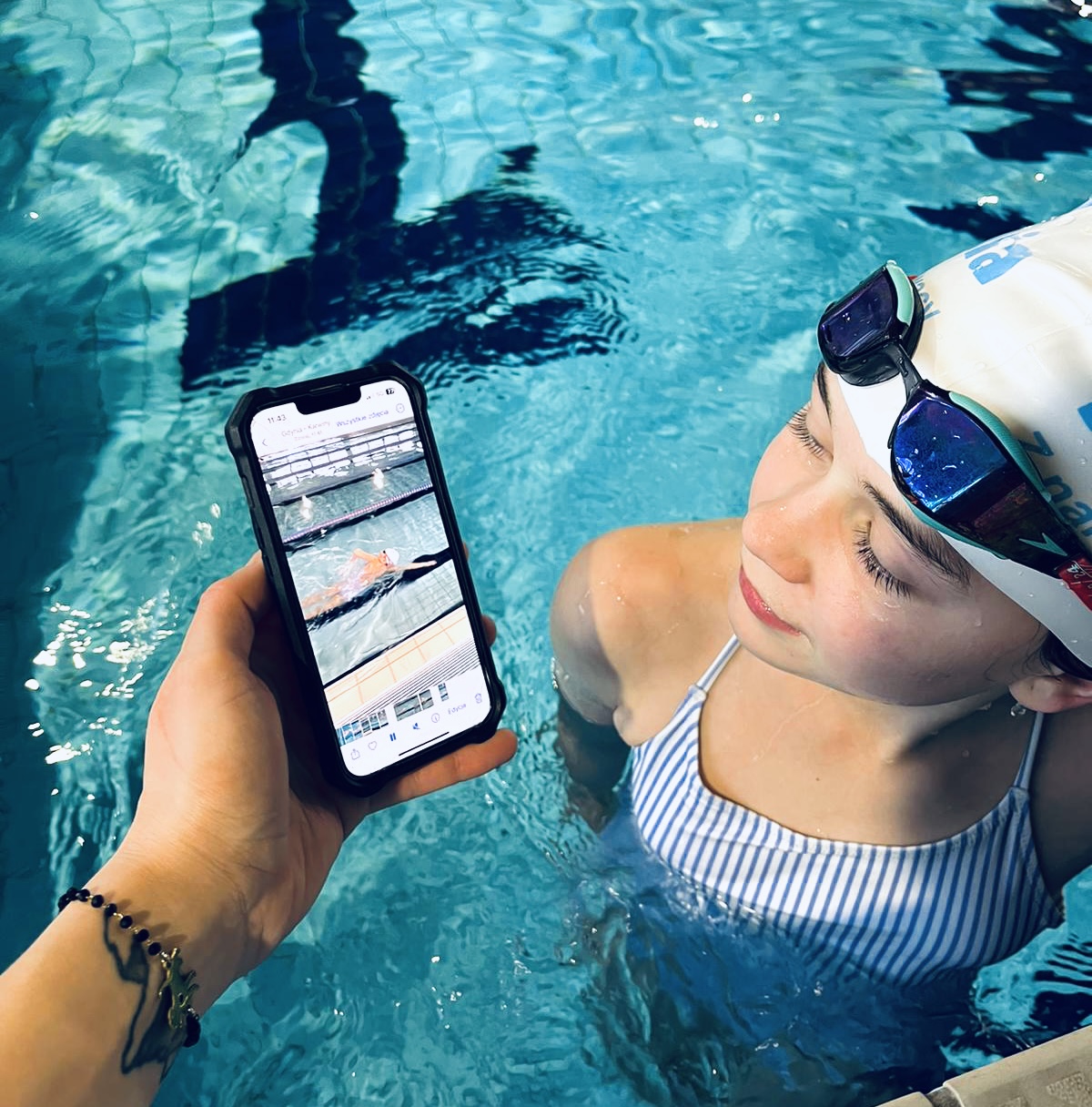 Dziewczynka w basenie spoglądająca na ekran smartphona z wideoanalizą pływania